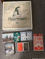 Top down photo of Huggermugger Mystery Word Game box with six decks of playing cards laid out below on carpet.