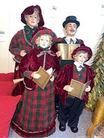 Photo of four Christmas caroling figurines dressed in traditional red and green clothing, holding songbooks.