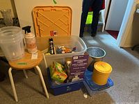 Wide view of lot showing orange storage bin, wooden stool, blue recycling bin, yellow container, metal bucket, and glass pitcher