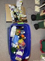 Wide shot showing two containers with various cleaning products inside, placed on the floor with a pair of boots nearby.
