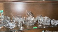 Shelf display of clear crystal and cut glass items including candy dishes, stemmed glasses, covered bowls, and a basket.