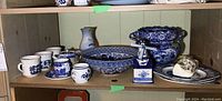 Shelf displaying various blue and white ceramic cups, plates, bowls, and jars including Royal Copenhagen jar and Wood & Sons cup and saucer.