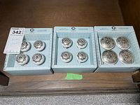 Photo of three boxes each containing a set of 4 drawer pulls. Left box has white ceramic pulls with decorative metal centers. Middle and right boxes have metal pulls with intricate raised patterns.