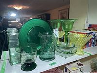 Photo of various green glassware items including a pitcher, plate, multiple bowls, and vases with hobnail diamond patterns.