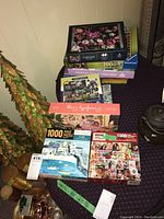 Full view of the 9 jigsaw puzzle boxes stacked on a table, with varied themes and brands visible.