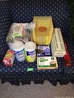 Photo of various kitchen and cleaning supplies including Lysol wipes, yellow storage bins, aluminum trays, and kitchen bags.