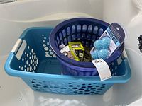 Three plastic laundry baskets shown stacked: two rectangular blue baskets with white handles and one round purple basket with vertical ridges. Also includes three sets of new plastic dryer balls in packaging in various colors and a mesh laundry bag.