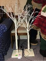Two white decorative light-up trees with wired branches, standing on square bases with visible power cords