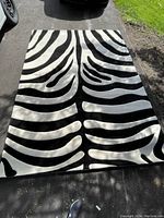 Unrolled zebra print rug laid flat on outdoor pavement showing full design and size.