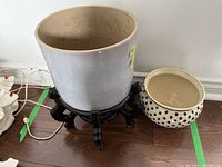 Two ceramic plant pots on the floor, one larger on black wooden stand and one smaller with blue polka dots beside it.