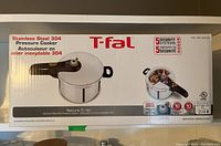 Photo of the front of the original boxed packaging showing the T-fal Secure 5 Neo stainless steel 304 pressure cooker with safety features.