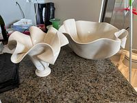 Set of two cream-colored Hilborn pottery pieces, a sculptural vase with curled petal edges on the left and a wavy-edged bowl on the right, shown on a dark countertop.