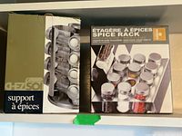 Original boxed Stokes 16 jar revolving spice rack and Chez Soi 12 jar fixed spice rack shown side by side on shelf.