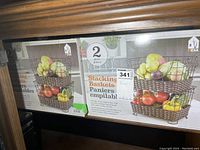 Photo showing two unopened 2-piece stacking basket sets in boxes. The baskets are brown woven plastic with open design.