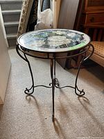 Full view of circular stained glass table showing floral and butterfly design on top and metal legs.