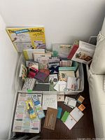 Photo showing plastic bin filled with assorted stationery items including a magnetic calendar and various notecards.