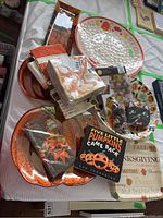 Photo showing large plastic Thanksgiving platter, packaged paper napkins, a tea towel, Halloween bowl, glass pumpkin plates, children's book and other assorted holiday items