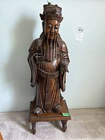 Front view of the full sculpture showing the detailed face and traditional robe, with tag visible on the wall.