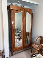 Front view of wardrobe showing two mirrored doors, carved wood frame and removable top section placed on top