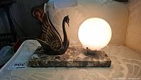 Full view of assembled lamp, lit, showing marble base, metal swan and glass globe.