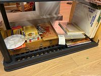 Artist canvases, paint tubes, wooden box, plastic palette, and other supplies on floor shelf.