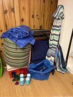Photo of the lot showing the two zero gravity chairs with blue fabric, green and beige striped cushion, a blue tarp, folded cooler, blue and white striped umbrella, plastic colored glasses and cups