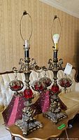 Pair of vintage cherub lamps on antique table with red glass details and lampshades, show overall look and scale compared to sofa.