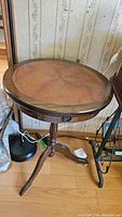 Full view of the antique round pedestal table showing leather top and wood base, placed against wallpapered wall.