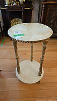 Front view of round marble plant stand with detailed gold metal grapevine motif legs and bottom marble shelf.