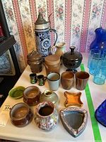 Overview of all pottery items including stein with lid, pitcher, cups, small vases, dishes, and jars on tabletop.