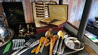 Full view of assortment showing gold plated hosting set, mother of pearl butter spreaders, ivory-handled steak cutlery set in cases, and other serving utensils.