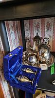 Full view of silver-plated tea and coffee service on tray with cream and sugar bowls, with salt and pepper shakers in blue velvet lined case in front.