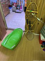 Wide shot showing green plastic toboggan, wooden snowshoes, and two tennis rackets