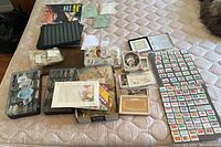 Overview view of the stamps, postcards, Canadian Millennium keepsake, album, and holders on mattress surface.