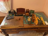 Photo showing vintage office supplies arranged on an antique wooden desk including leather blotter, letter holder, inkwells, rulers, pen box, and other small accessories.