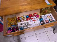 Drawer holding multiple boxes and loose vintage Christmas ornaments in various colors and styles including gold, silver, red, blue, and pink balls as well as clip-on birds.