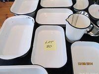 Top view of varied sizes of white enamel pans with black rims and measuring jug.