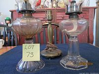 Two antique oil hurricane lamps with glass fonts and chimneys, and a Pairpoint lamp base with visible wiring and broken glass shade on table