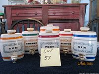 Front view of all six ceramic casket dispensers labeled Rum, Sherry, Port, Scotch, Gin with cork stoppers and metal spouts.