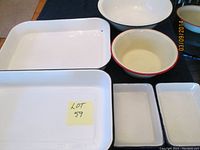 Overall view of five enamelware pieces: three rectangular trays in white enamel and two round bowls, one cream with red rim.