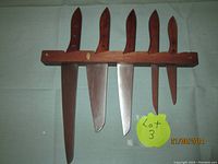 Photo showing five knives held in a wooden wall holder, blades and handles visible.