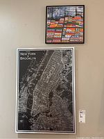 Two framed wall art pieces on a beige wall: larger rectangular black and white NYC & Brooklyn map on aluminium, smaller square colorful vintage print above.