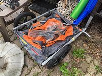 Angled side view of the folded bicycle cart attachment showing the frame, wheels, and fabric seat area