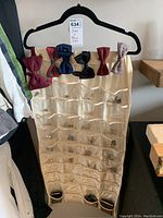 Full view of beige fabric hanging organizer with seven bowties clipped at the top and multiple cufflinks inside clear pockets