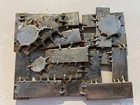 Front view of a welded metal wall sculpture showing interconnected flat plates, circular and irregular shapes with visible welds.