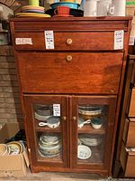 Front view of vintage wood cabinet desk showing top drawer, drop-down desk, and glass-door cupboard with dishes inside