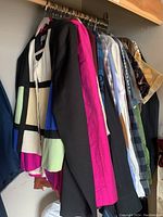 Photo of assorted tops and dress shirts hanging on rack showing a variety of colors including white, purple, black, green, blue, and plaid patterns in sizes small and medium.