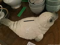 Cream ceramic seal piggy bank with coin slot on back, showing textured details.