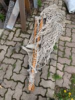 Rope hammock with wooden spreader bars laid on paving stones, showing braided rope net and wooden slats.