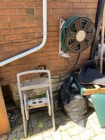 Wide angle view of two hose reels and a garden hose coiled around them, set against a brick wall with some clutter around